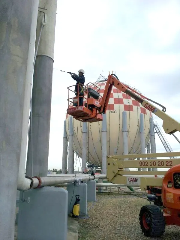 Operario con plataforma elevadora junto a una esfera de gas durante el ignifugado de sus patas